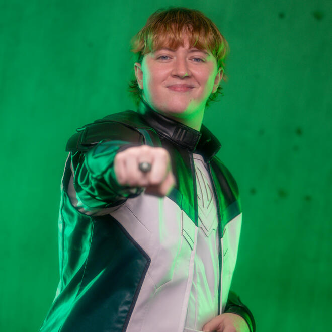 Brie, dressed as Guy Gardner from Superman (2025), with his fist pointed towards the camera to showcase his Green Lantern ring.