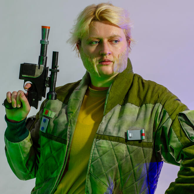 Brie, dressed as Rebel Alexsandr Kallus from the Star Wars Rebels, holding a blaster up next to his face.